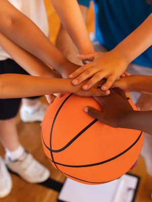 Close-up of Schoolkids forming hand stack on basketball at basketball court in school